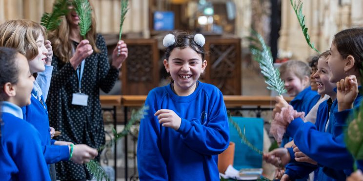 Children in two lines holding palm leaves while a child walks through smiling