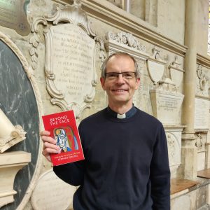A reverend holds a book with a red cover, called Beyond the Face, by Stephen Girling