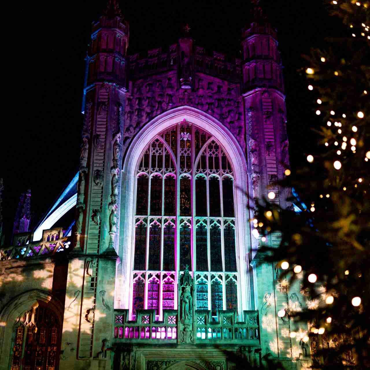 Bath Abbey lit up with colourful lights and a Christmas Tree with gold lights